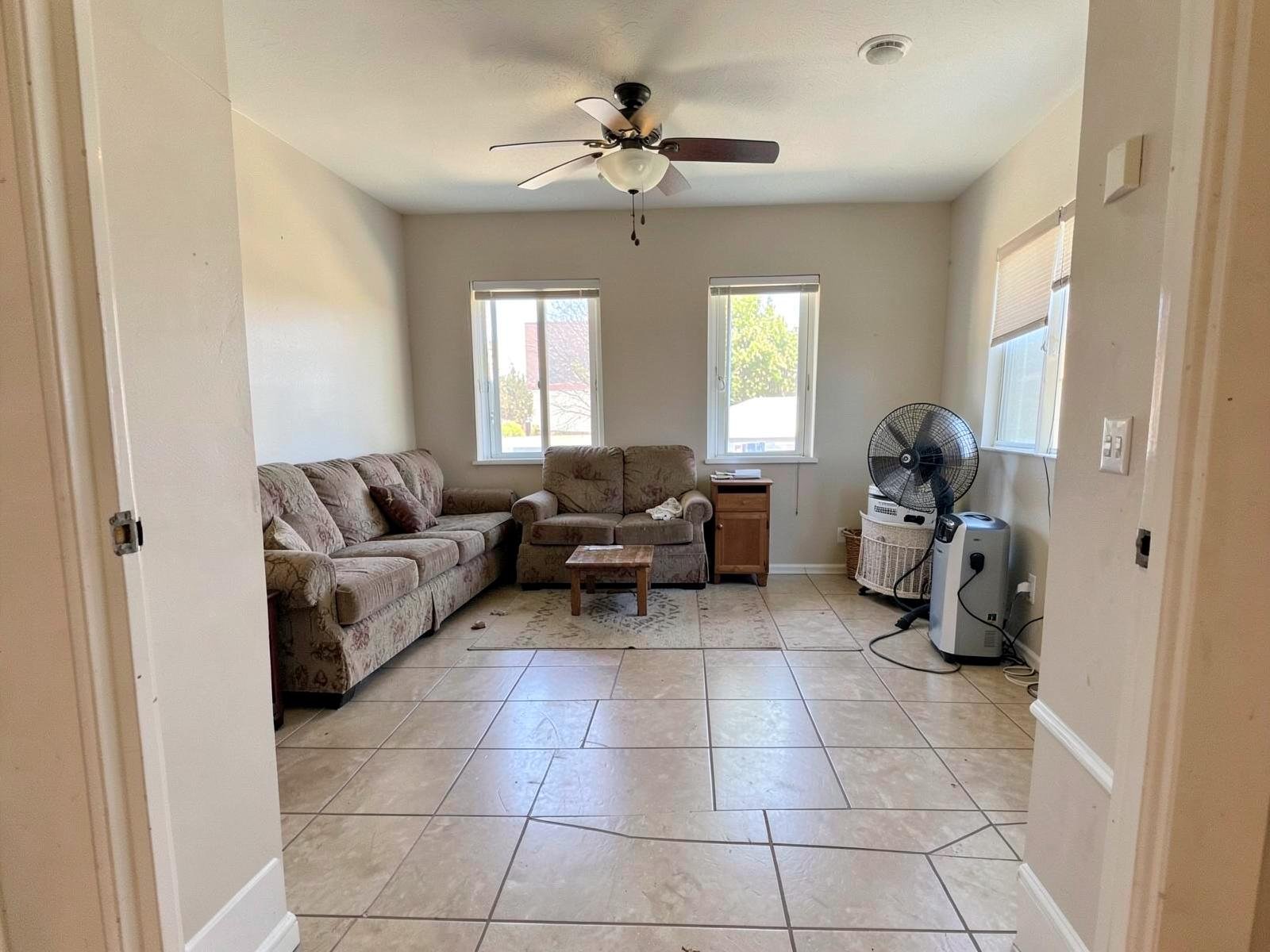 After flood cleanup — the same living room from the identical doorway angle, tile floor clean and dry, walls repainted with no mud line, air mover and dehumidifier finishing the dry-out.