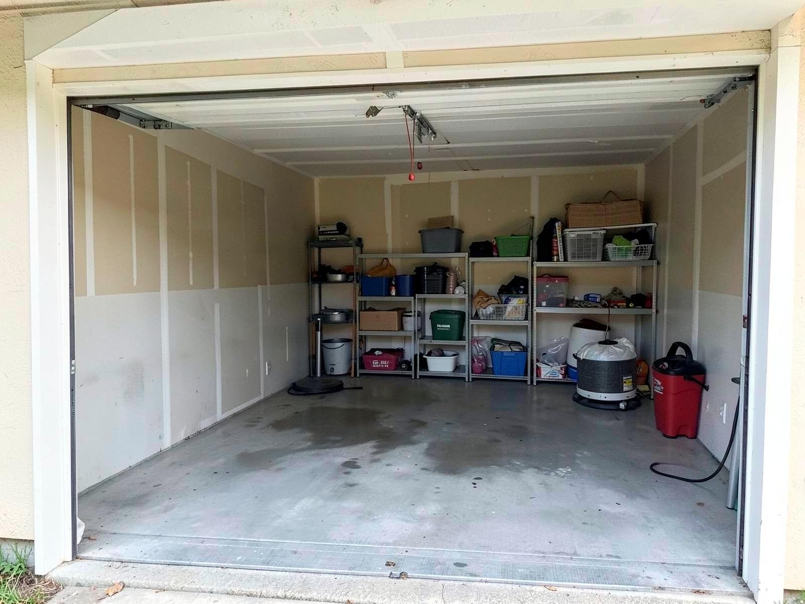 After flood cleanup — the same garage from the identical angle, slab pressure-washed clean and dry, walls repaired and repainted, storage restocked on new shelving.