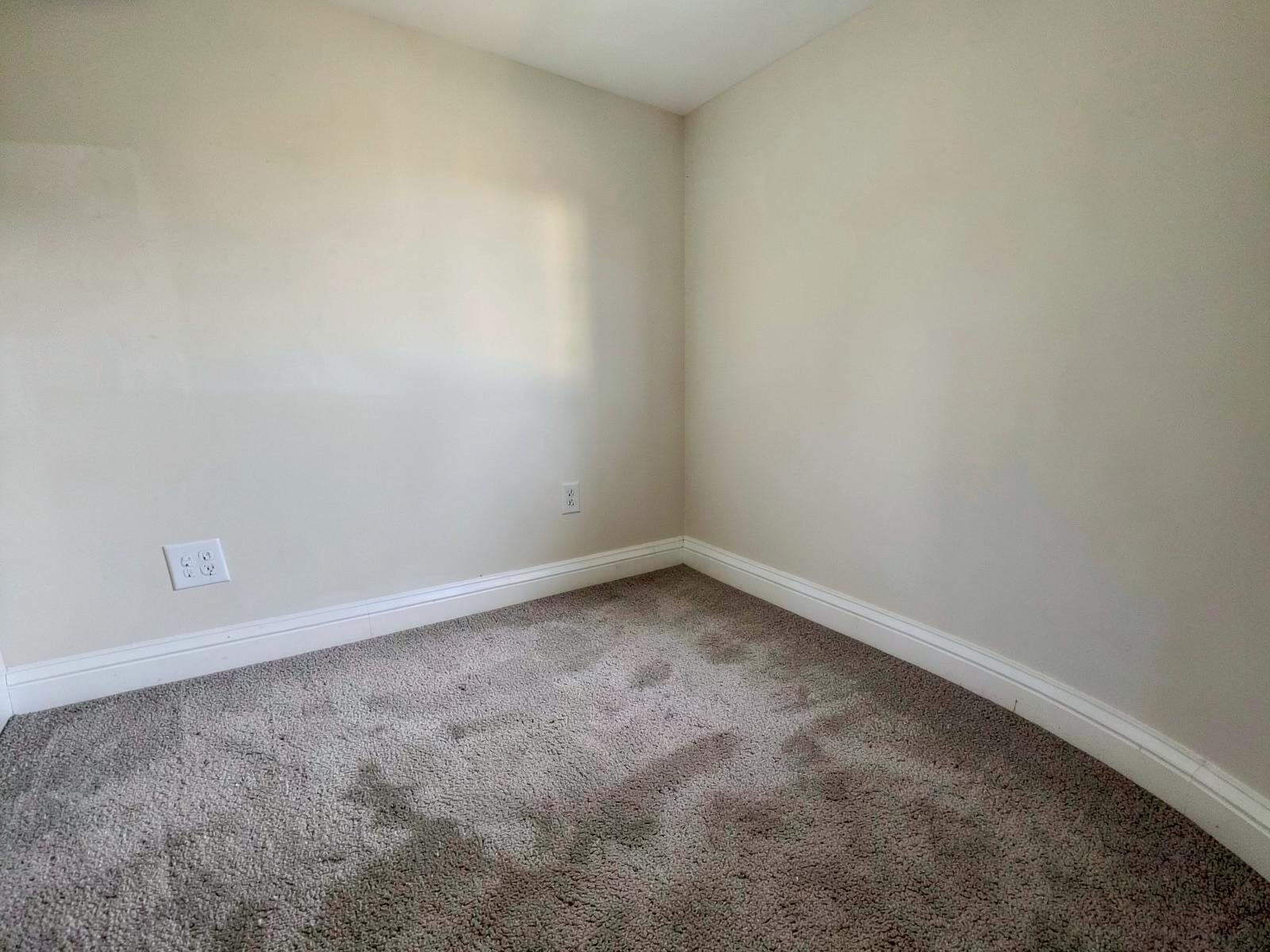 After flood cleanup — the same bedroom wall base from the identical angle, new dry carpet, drywall replaced and repainted, new baseboard installed flush.