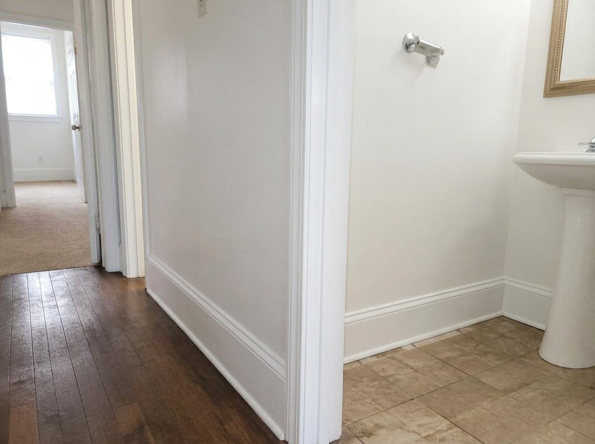 Job #WD-2408-042 after restoration — same hallway and bathroom doorway, same camera angle as the before photo. Bright white walls, clean fresh baseboards, wood floor and tile clear — no visible mold or staining.